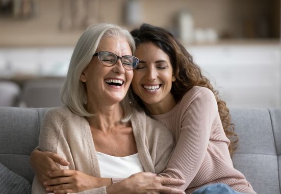 שיחה על בריחת שתן אצל ההורים, אמא ובת מבוגרות מחובקות על ספה שמחות
